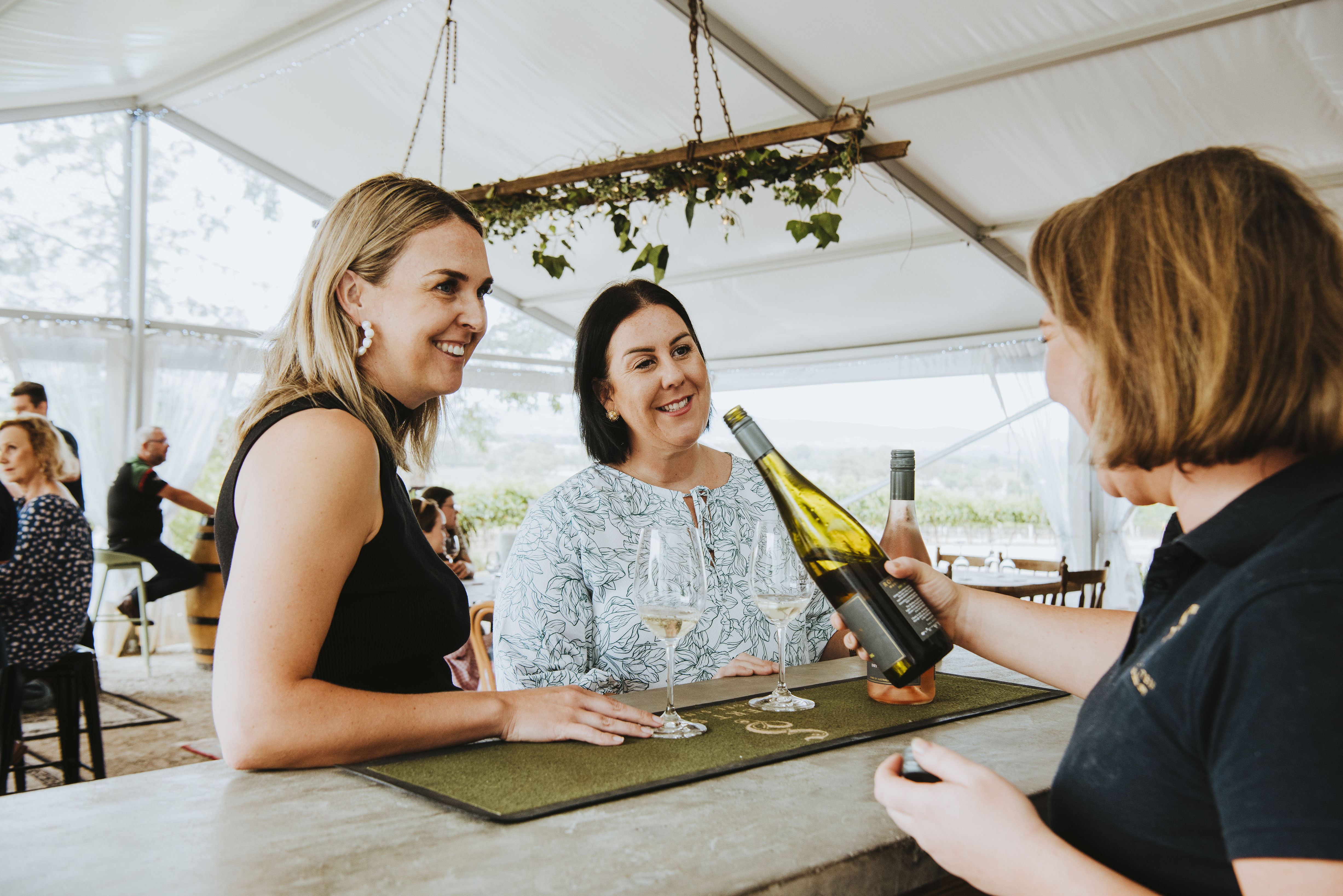 Two women talking with bartender holding a wine bottle